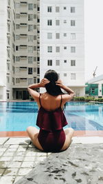 Rear view of man sitting on swimming pool against building