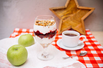 Cherry yoghurt parfait with crispy granola on top in a wine glass and cup of tea