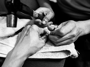 Cropped hand of man repairing wristwatch with male friend at home