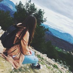 Woman sitting on mountain against sky