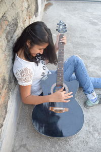 Young woman playing guitar against brick wall