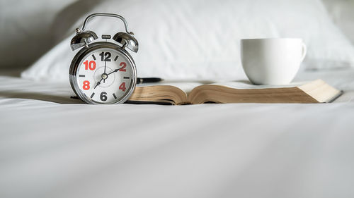 Close-up of clock with book and coffee cup on bed