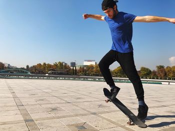 Young man skateboarding on walkway against clear blue sky