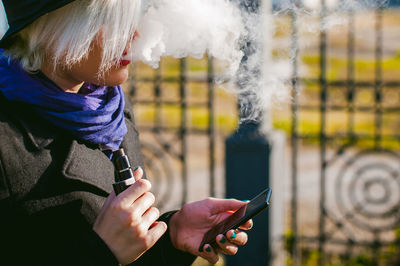 Young woman using mobile phone while smoking at park