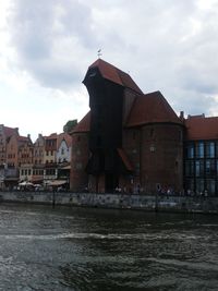 Buildings at waterfront against cloudy sky