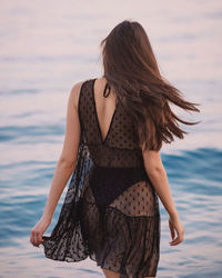 Rear view of woman standing in sea against sky