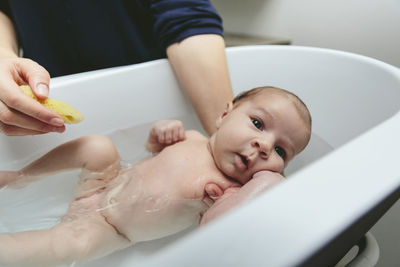 Midsection of mother bathing son in bathtub at bathroom