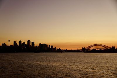 Silhouette buildings by sea against sky during sunset