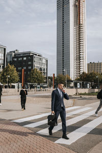 Businessman talking through smart phone while walking on zebra crossing at street in city