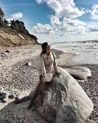 Woman sitting on rock at beach against sky