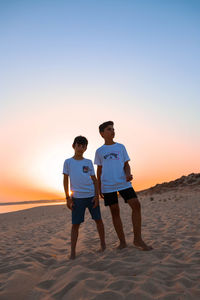 Full length of friends standing on beach against sky during sunset
