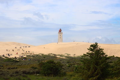 Lighthouse on sand dune against sky