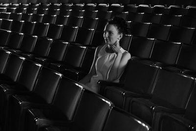 Young woman looking away while sitting on chair in auditorium