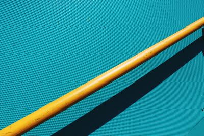 High angle view of yellow metallic railing with shadow on turquoise wall during sunny day