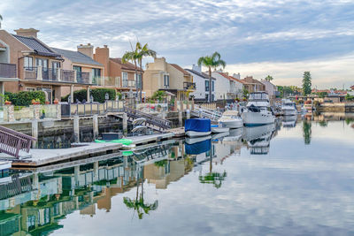 Boats moored in canal by buildings against sky