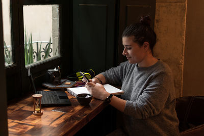 Young woman looks at her phone while studying in a retro pub