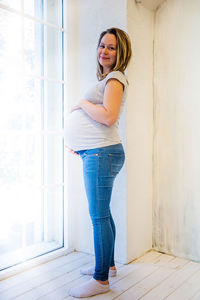 Portrait of pregnant woman standing against window at home