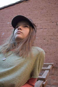 Portrait of young woman using mobile phone against brick wall