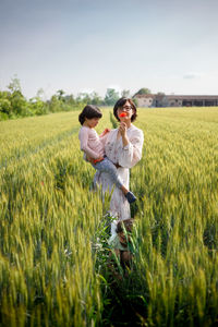 Mother holding daughter in her arms standing in grain field