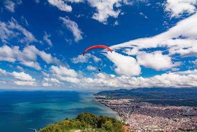 Parachute flying over cityscape and sea against cloudy sky