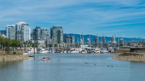 Boats moored in lake by city against sky