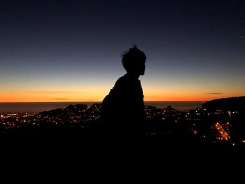 Silhouette man looking at cityscape against sky during sunset