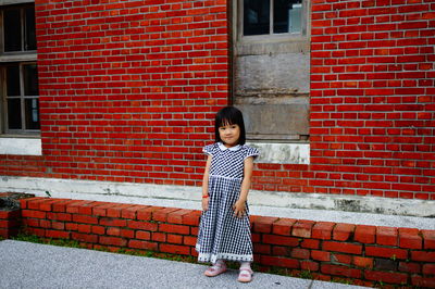 Portrait of girl standing against red brick wall