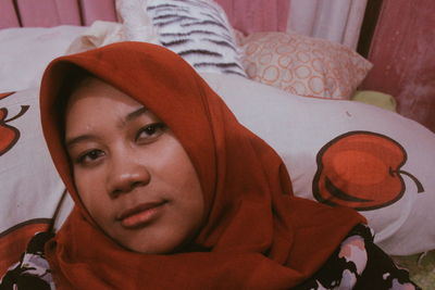 Close-up portrait of young woman wearing headscarf on bed at home