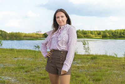 Portrait of beautiful woman standing by lake against sky