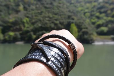 Cropped hand with black bracelets against river on sunny day