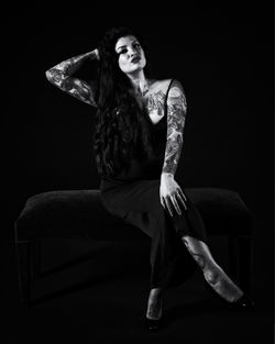 Young woman looking away while sitting against black background