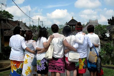 Rear view of friends with arms around standing on road