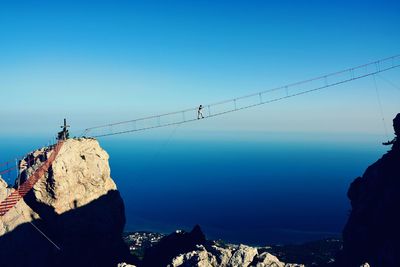 Person walking on bridge against blue sky during sunny day