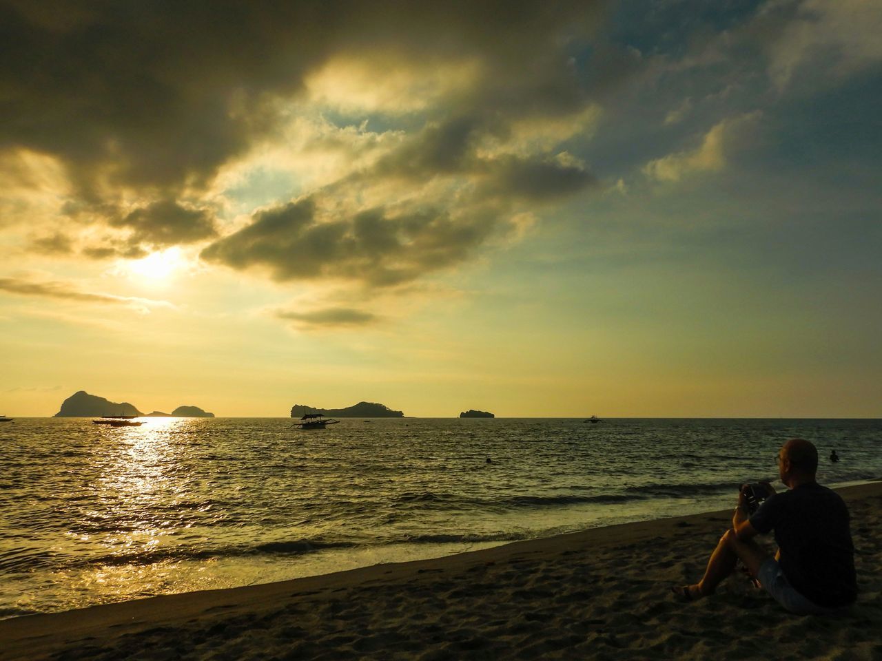 PEOPLE SITTING ON BEACH DURING SUNSET