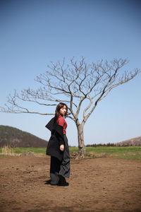 Side view of young woman standing on field against clear sky