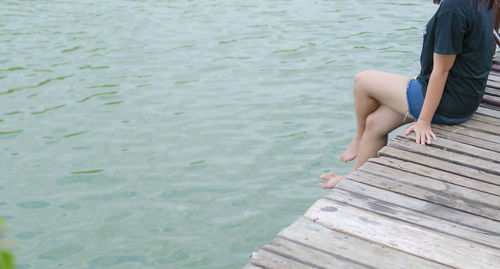 Low section of man sitting on pier over lake