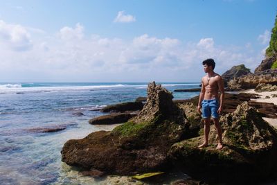 Shirtless man standing at beach against sky