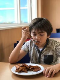 Boy eating potato chips while sitting on chair at restaurant