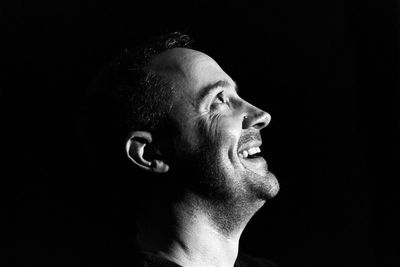 Side view of smiling man against black background