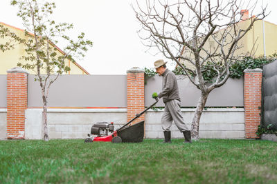 Male mowing the grass with a lawn mower in the garden on the background of buildings