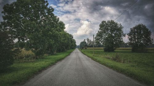 Road amidst trees on field against sky