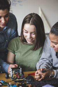 Smiling female teacher and high school teenage students preparing robot on desk in classroom