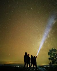 Silhouette friends with illuminated flashlight against star field