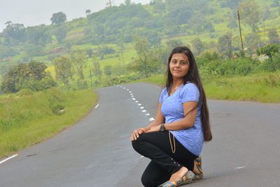 Portrait of smiling young woman on road against trees