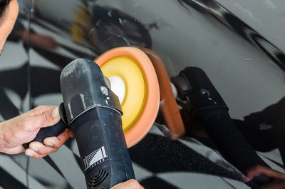 Cropped hands of man cleaning car with equipment in garage