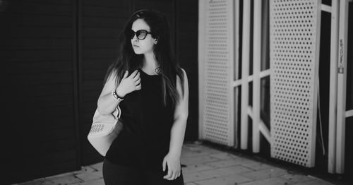 Young woman wearing sunglasses standing against wall