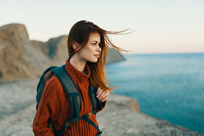 Young woman standing at beach against sky