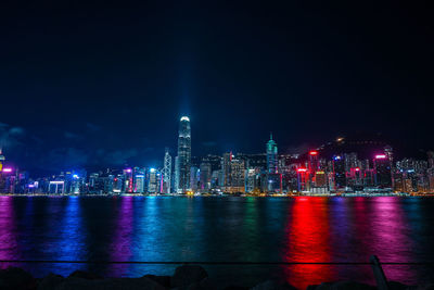 Illuminated buildings by river against sky at night