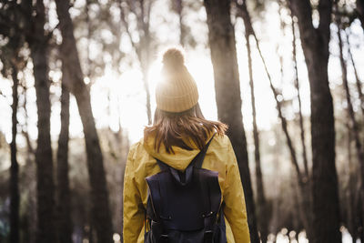 Rear view of woman standing by tree trunk in forest