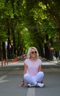 Portrait of young woman sitting on road against trees